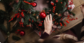 Decorative wreath with red ornaments on a wooden surface, with a hand adjusting the wreath. Floral Workshop