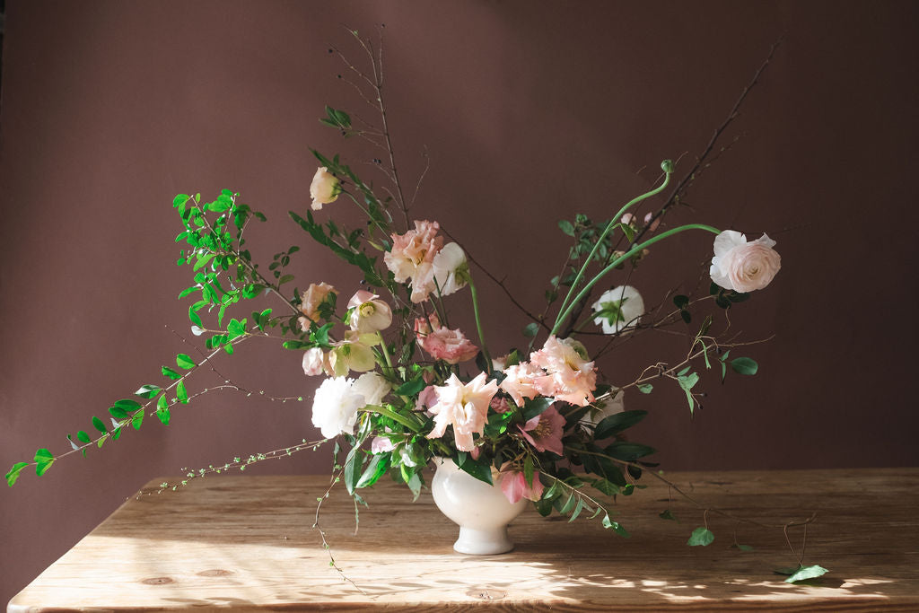 Large garden style floral arrangement in a white vase on a wooden table with premium flowers including ranunculus, lisianthus, spirea and hellebores. Perfect for small and intimate weddings in North Alabama.