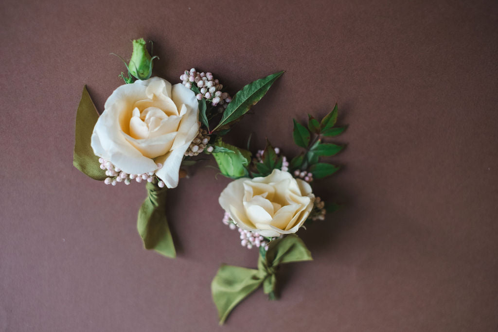 Two white roses with green leaves on a brown background.  Wedding flowers by The Dreamt Garden. Madison AL florist.